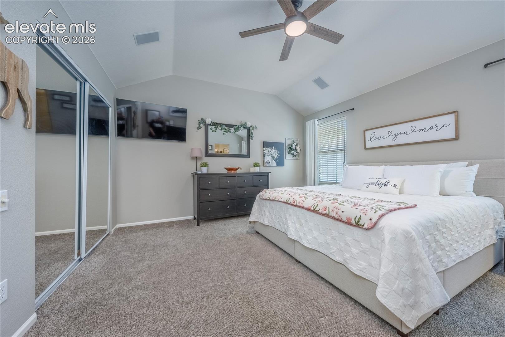 Vaulted ceiling with a central multi-blade ceiling fan, wall-to-wall carpeting, and sliding mirrored closet doors