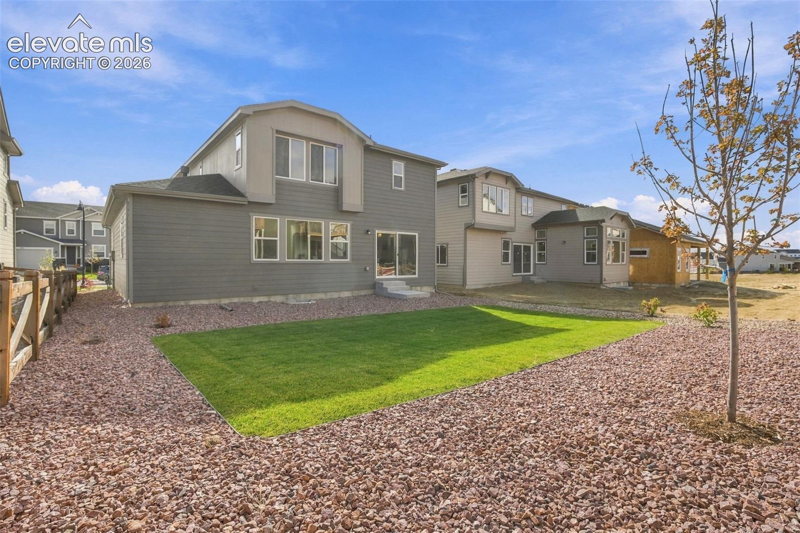 Exterior featuring lap siding, multi-level architectural roofline, manicured lawn, gravel landscaping, and wood-paneled perimeter fencing