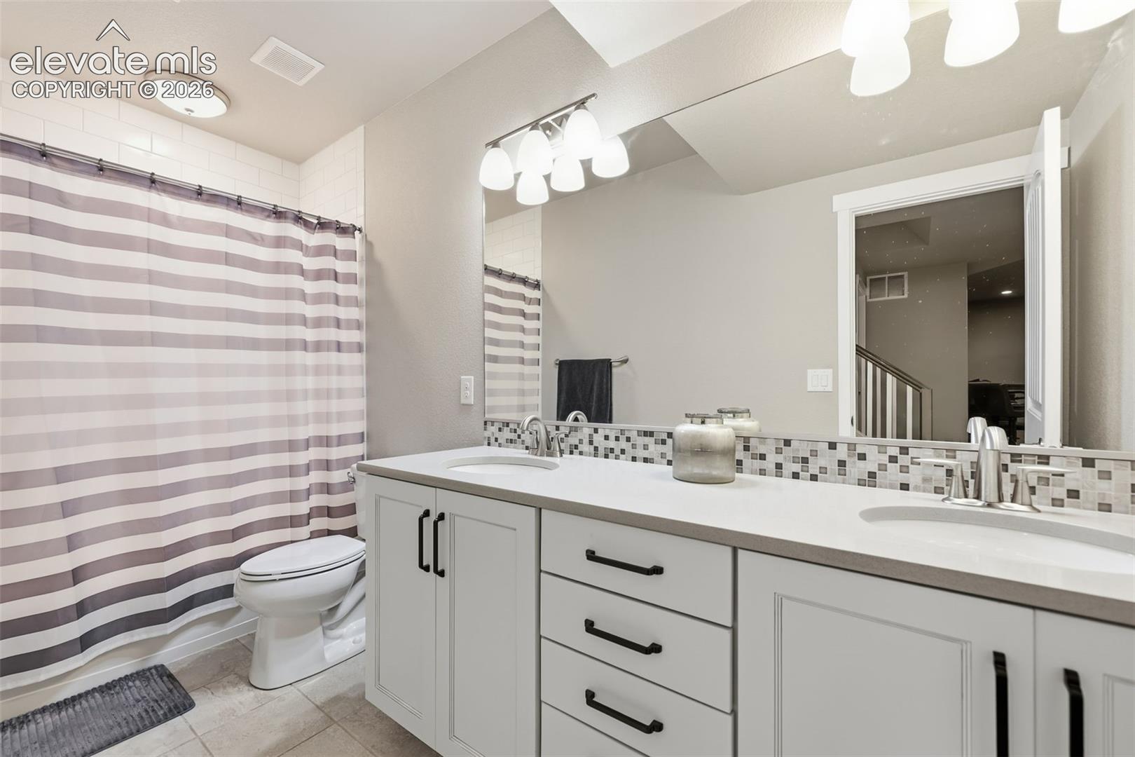Double vanity with undermount sinks, light stone countertops, and white cabinetry.