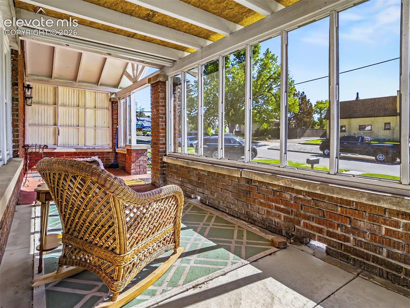 Enclosed front porch featuring brick knee walls, expansive windows, a concrete floor, and a slatted ceiling