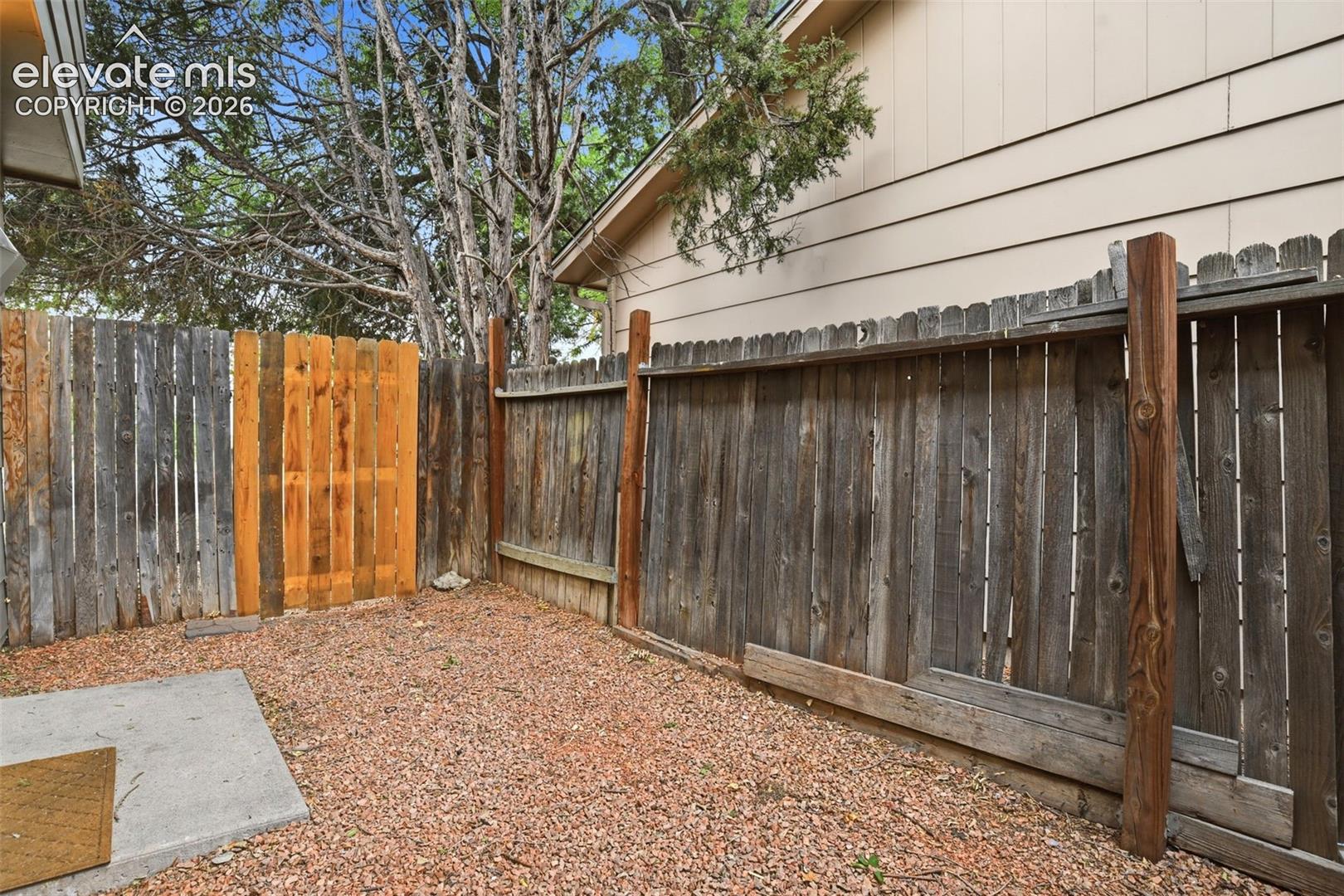 Enclosed backyard space featuring a wood fence, gravel ground covering, and a concrete pad