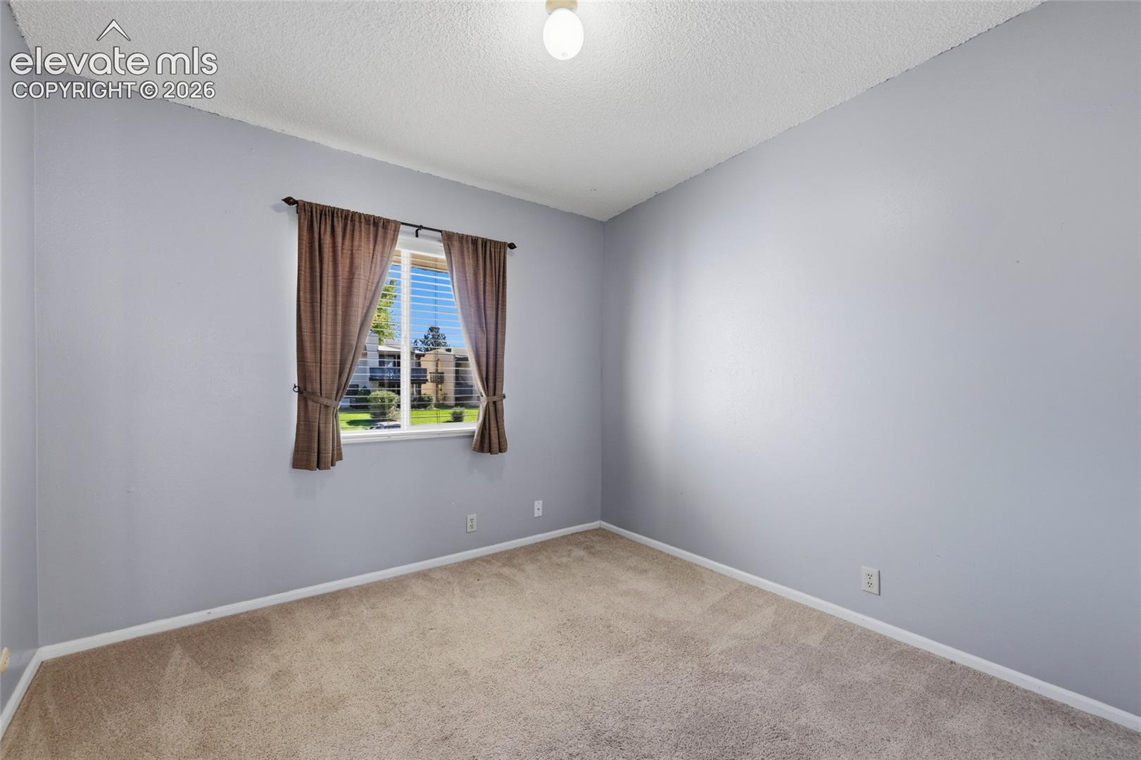 Neutral-toned interior room featuring wall-to-wall carpeting, a single window, and textured ceiling finish