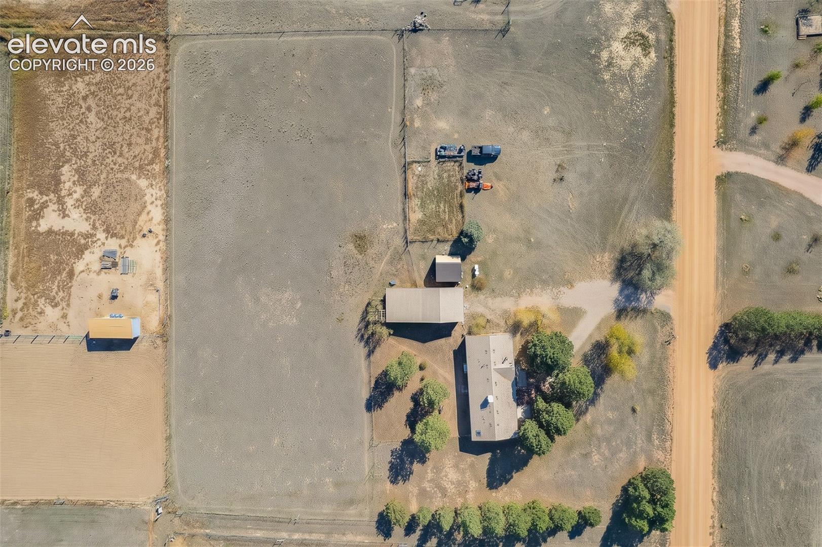 Aerial view of expansive property featuring a primary residence, detached outbuilding, fenced enclosure, and mature trees