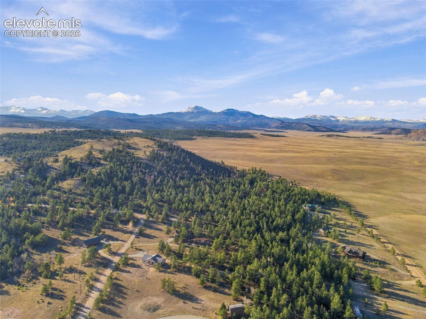 Aerial perspective of expansive acreage featuring mature evergreen forest, rolling terrain, and snow-capped mountain range backdrop