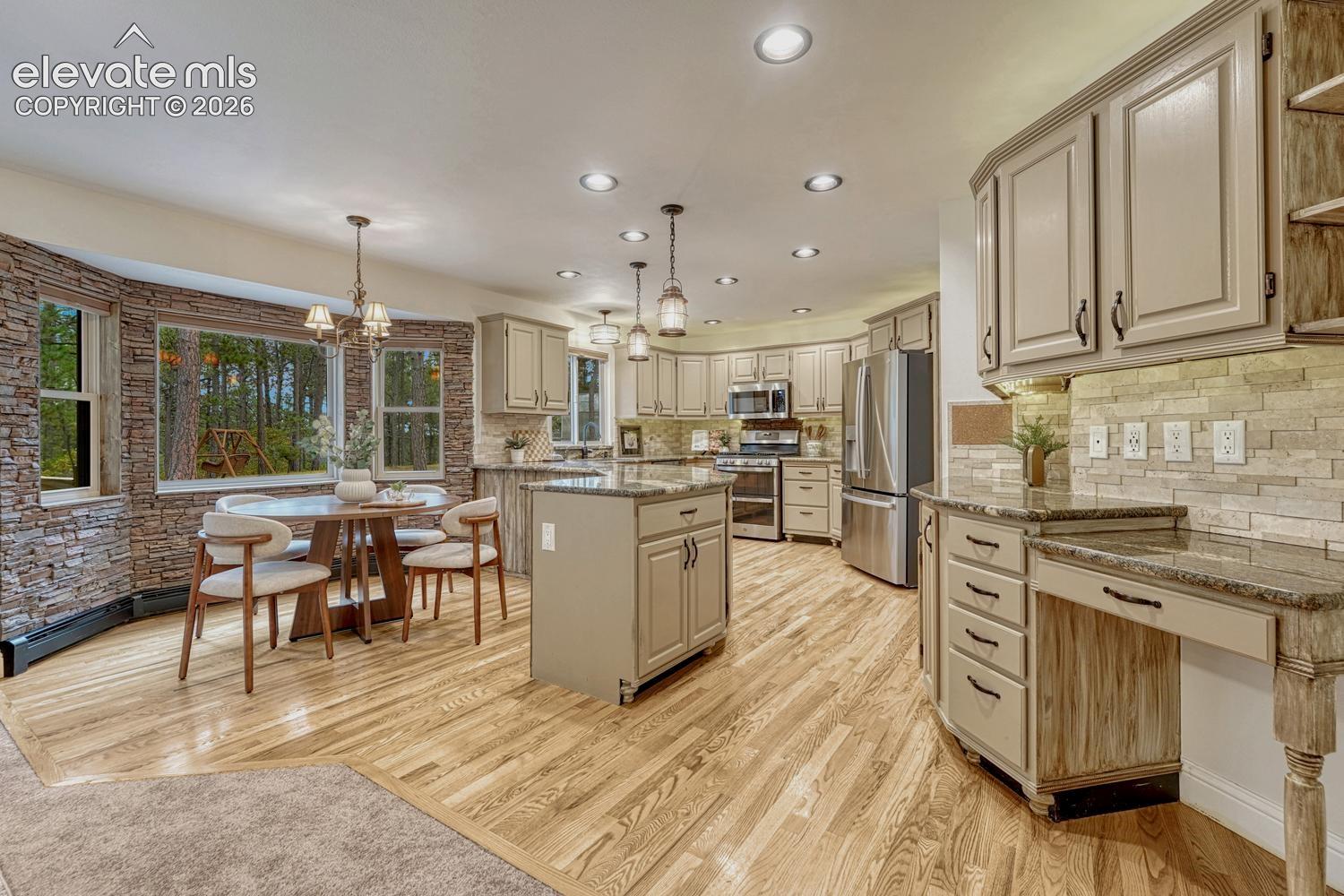 Kitchen featuring wood-finish flooring, a central island with cabinetry, stacked stone wall accents, recessed lighting, and a built-in workstation