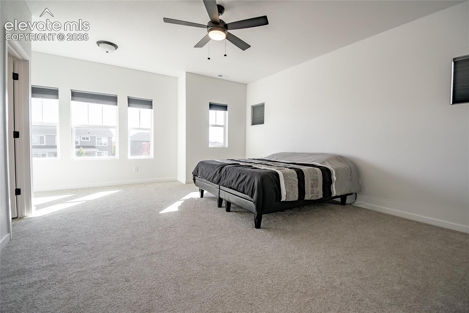 Expansive room featuring neutral wall-to-wall carpeting, multiple windows with integrated shades, a multi-blade ceiling fan, and recessed lighting