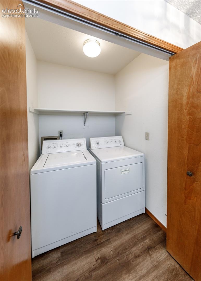 Dedicated laundry area featuring wood-finish flooring, overhead lighting, and an integrated storage shelf