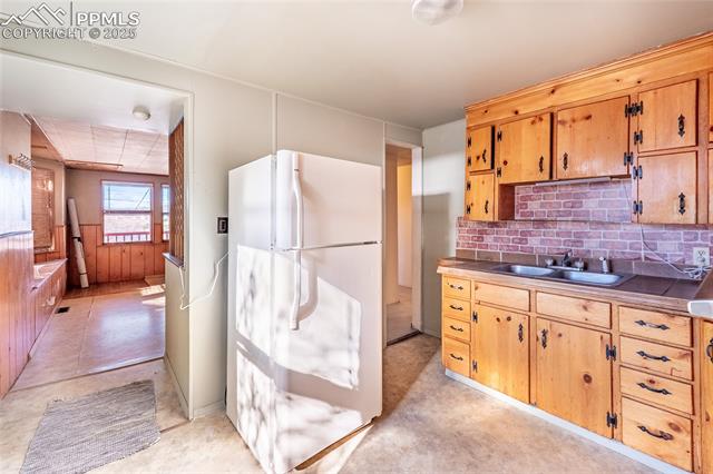 Kitchen with freestanding refrigerator, tasteful backsplash, wood walls, wainscoting, and light countertops