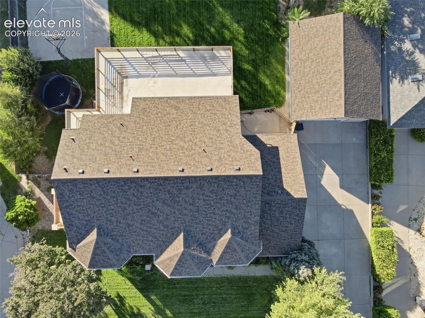 Expansive property featuring a multi-gabled roofline, concrete driveway, lush green lawn, and mature trees