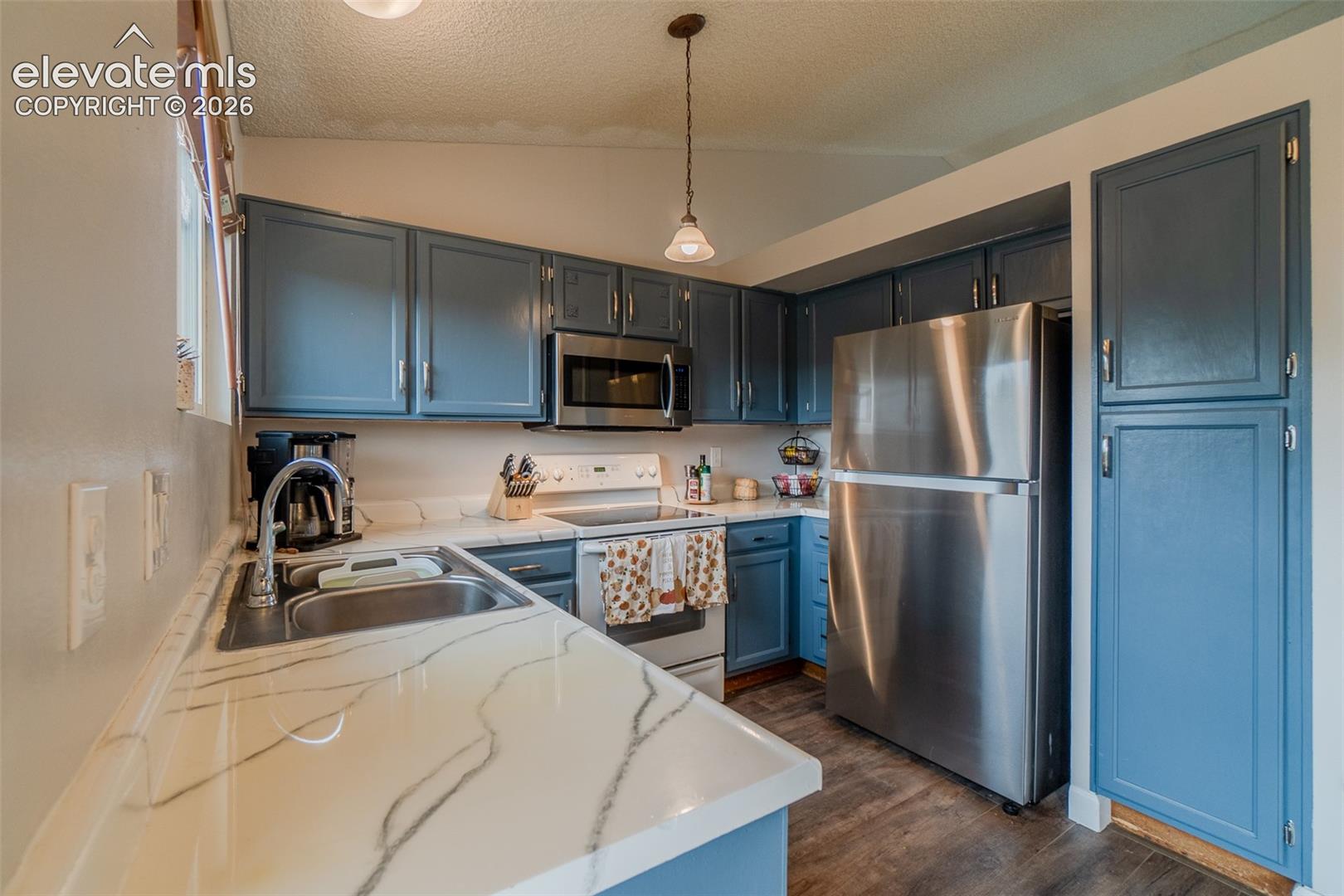 Kitchen with blue cabinetry, pantry, white countertops with dark veining, stainless steel appliances, and wood-finish flooring