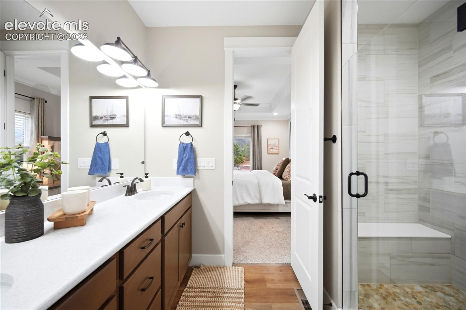 Bathroom featuring a dual-sink vanity with white countertops, wood-finish cabinetry, a walk-in shower with floor-to-ceiling tile, a built-in shower bench, and a four-light vanity fixture