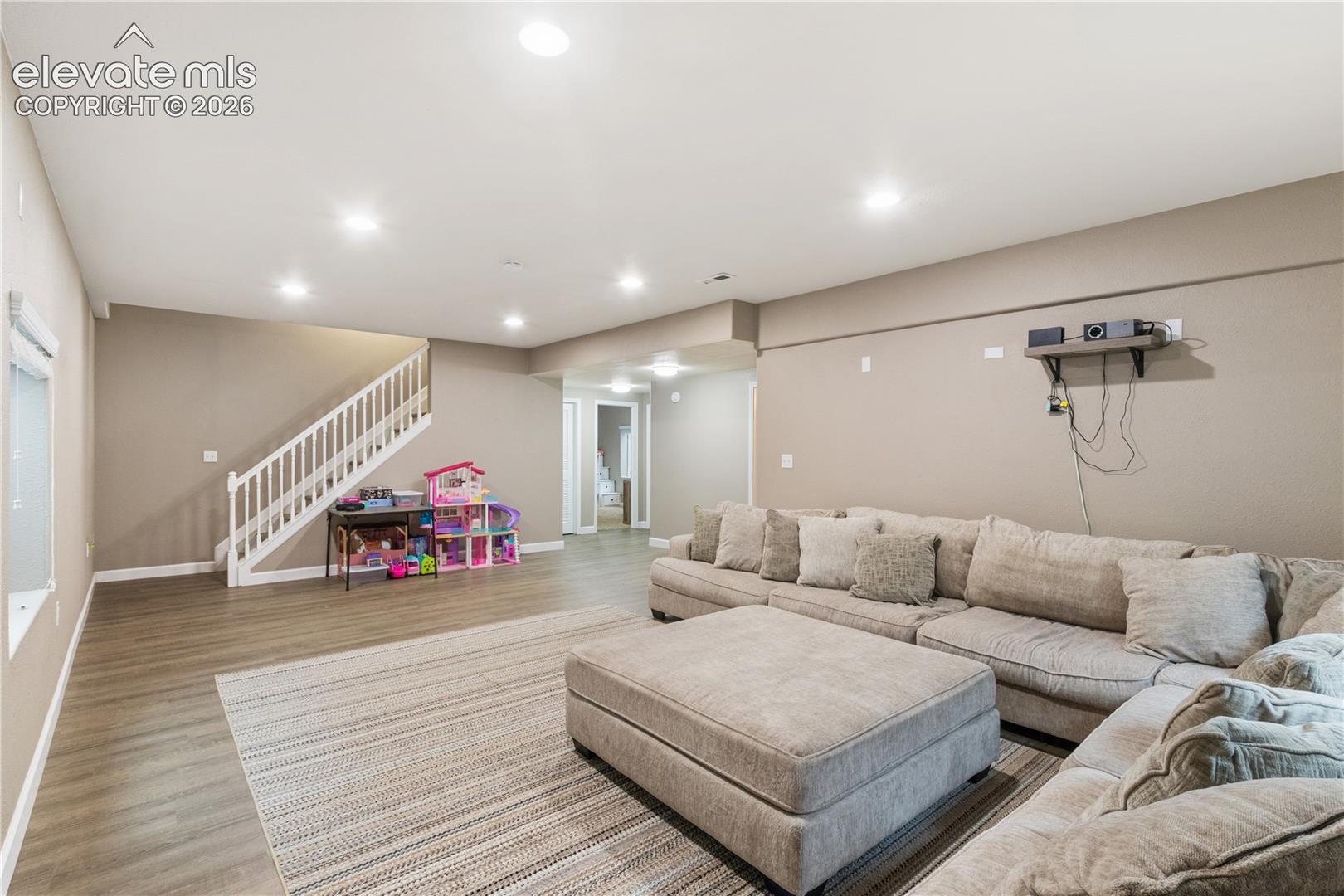 Open-concept interior featuring wood-finish flooring, recessed lighting, and a white staircase with a wooden handrail