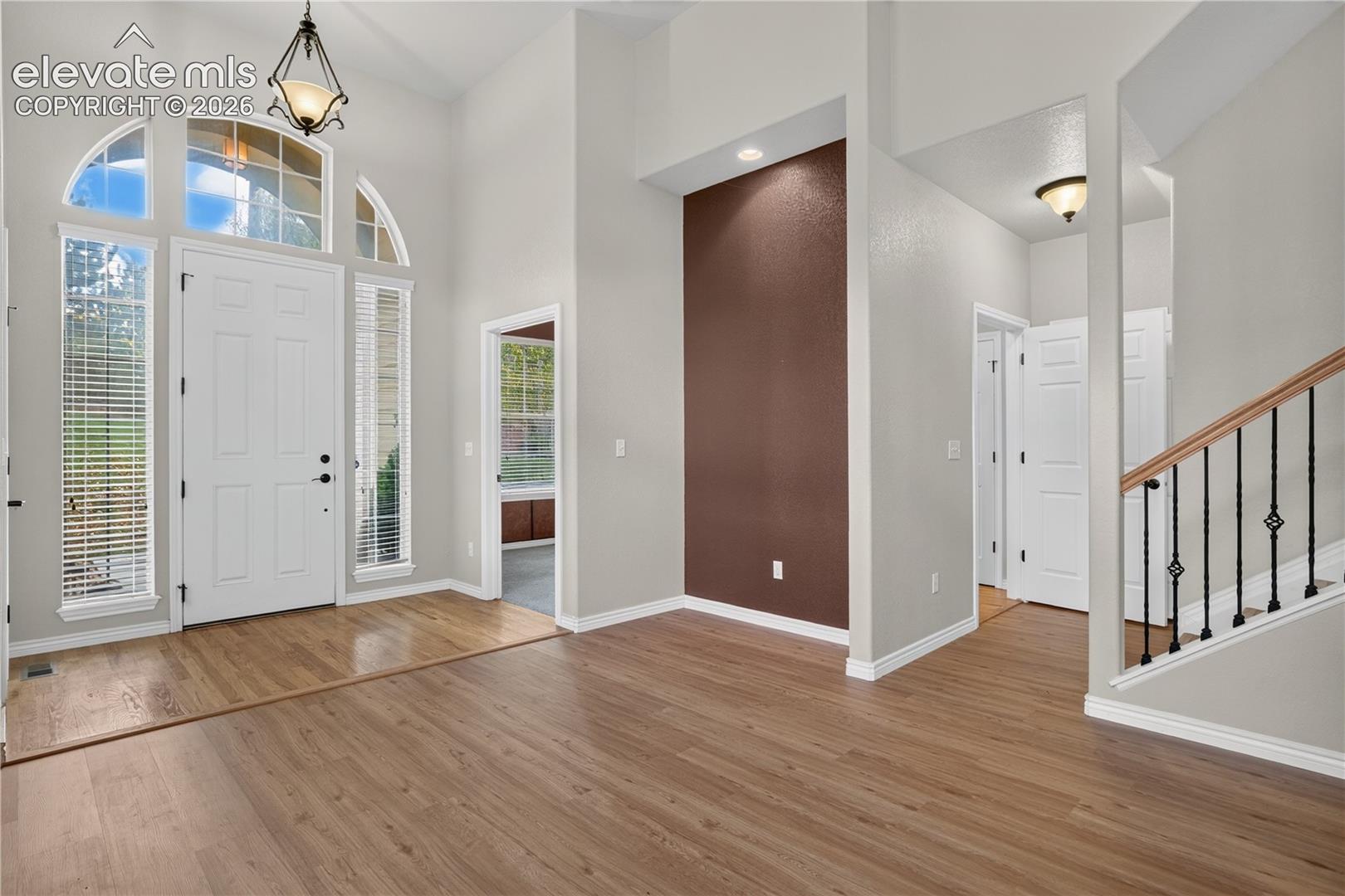 Foyer featuring soaring ceilings, wood-finish flooring, an arched transom window, a dark accent wall, and a staircase with metal balusters