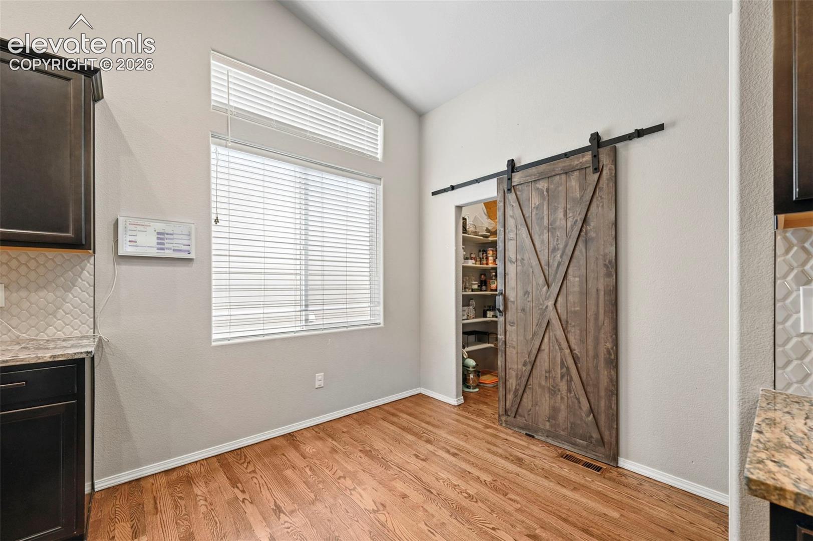 Vaulted ceiling, sliding wood-finish barn door, wood-finish flooring, and walk-in pantry