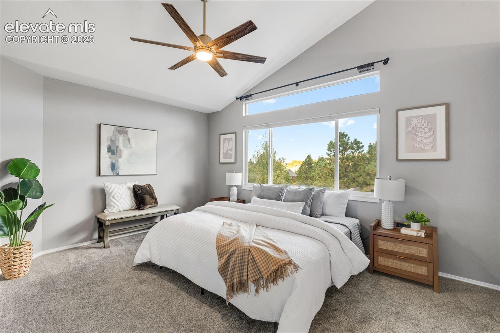 Vaulted ceiling featuring a central multi-blade ceiling fan, large picture window with an integrated transom, and carpeting