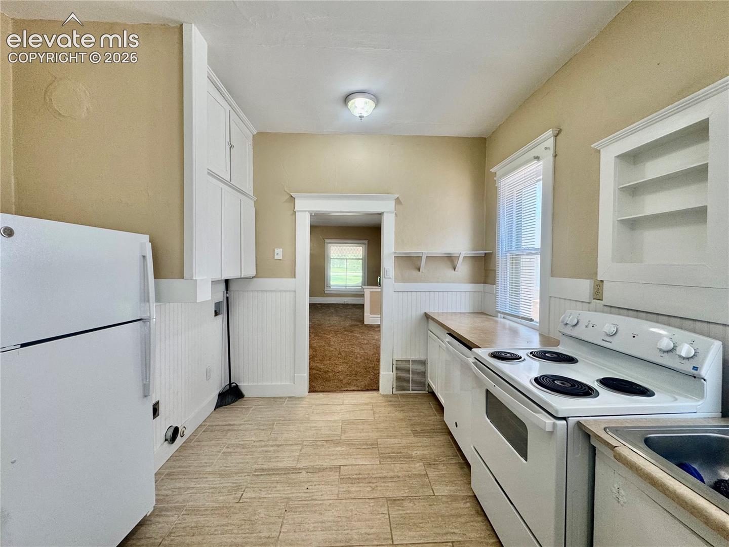 Kitchen featuring tile flooring, white cabinetry, integrated appliances, and a wood-finish countertop