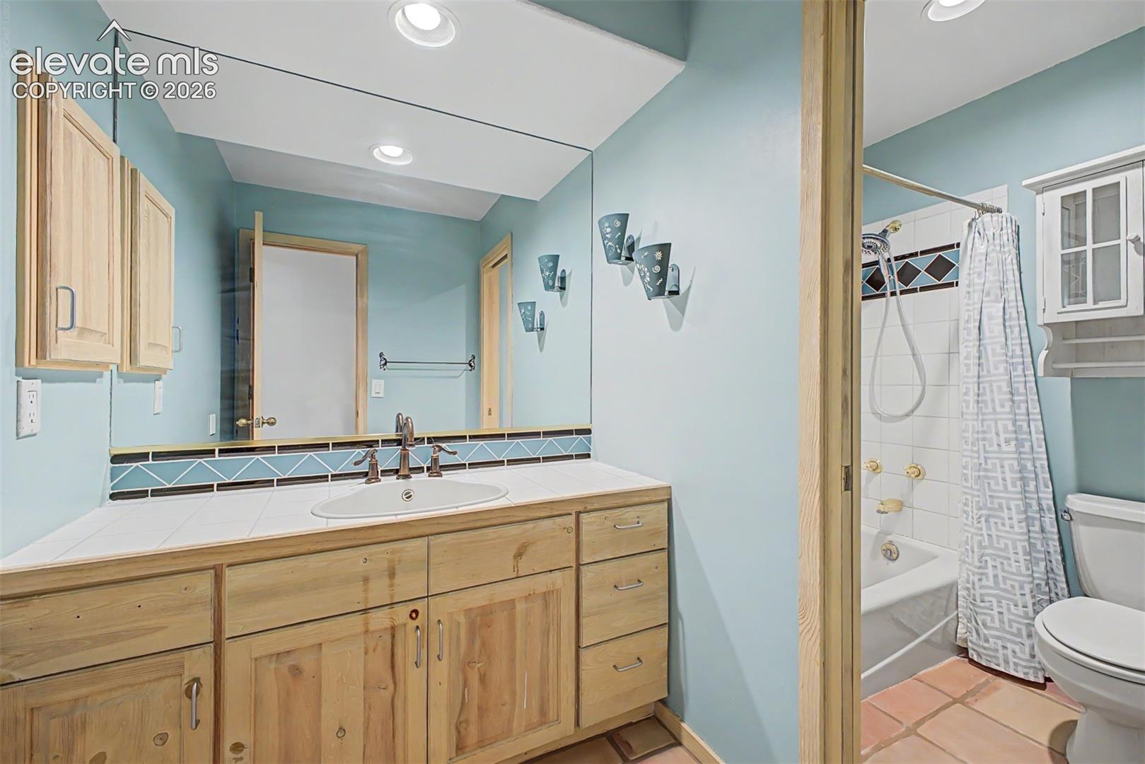 Wood-finish vanity with an integrated sink, large wall mirror, and recessed lighting