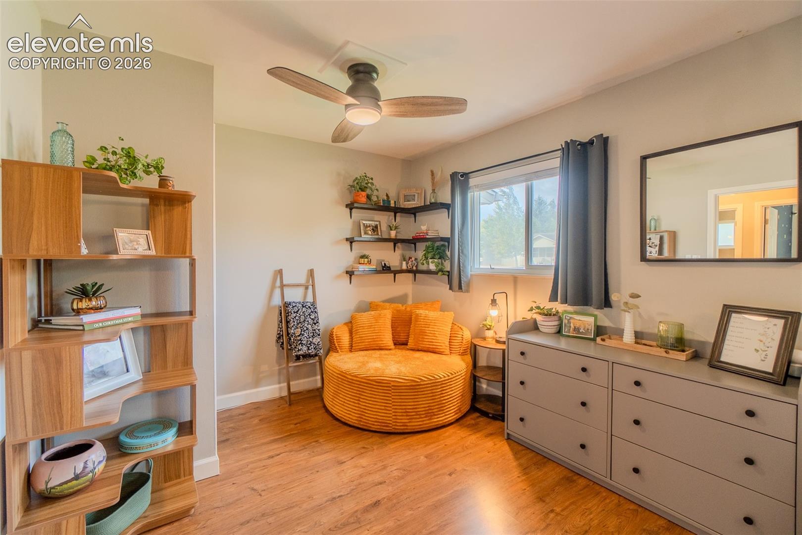 Room featuring wood-finish flooring, a ceiling fan, and corner-mounted floating shelving