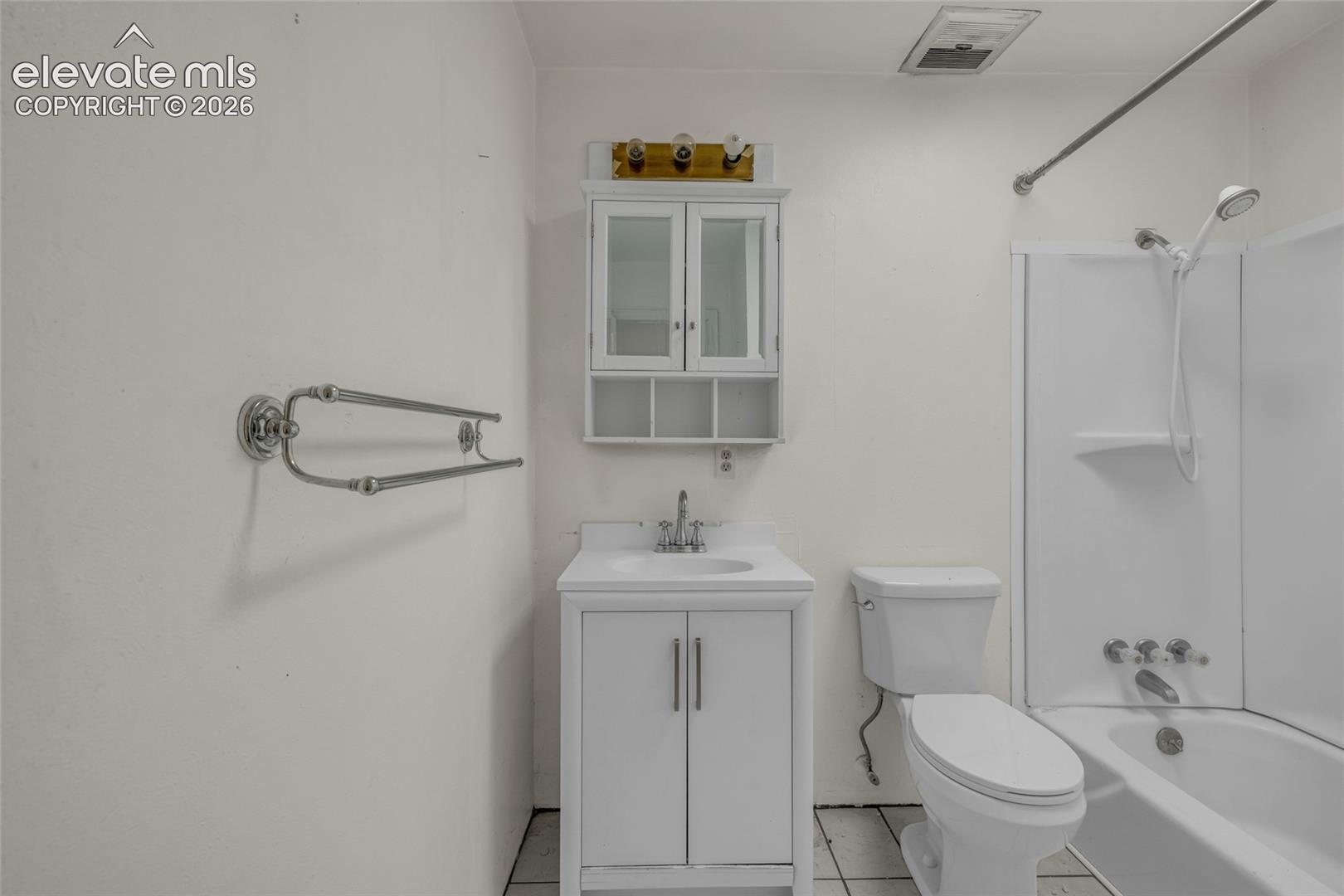White vanity with integrated sink, coordinating wall-mounted medicine cabinet, toilet, and a white bathtub with shower fixture
