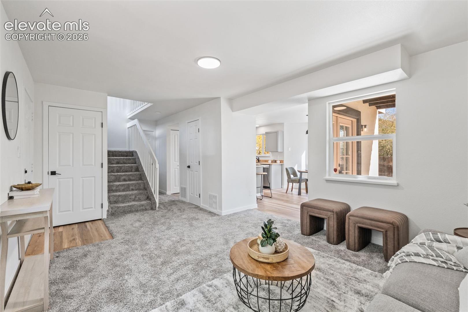 Neutral-toned carpeting, wood-finish entryway flooring, carpeted staircase with white railings, and oversized window with white trim