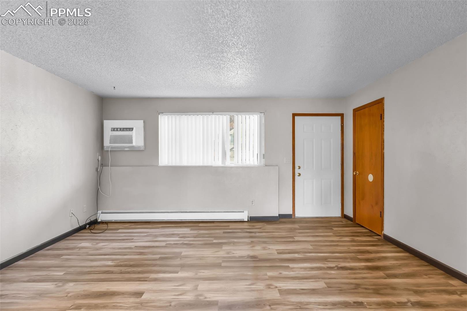 Empty room featuring light wood-style flooring, a textured ceiling, baseboard heating, and a wall mounted air conditioner