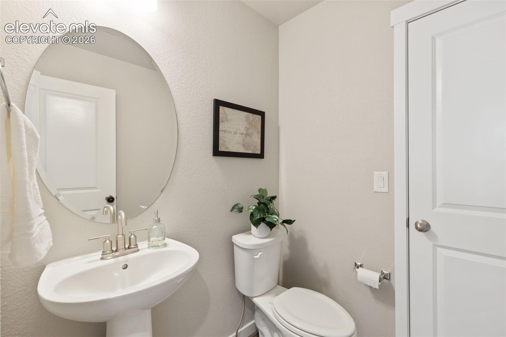 Pedestal sink with brushed nickel faucet, oval mirror, and light-colored walls