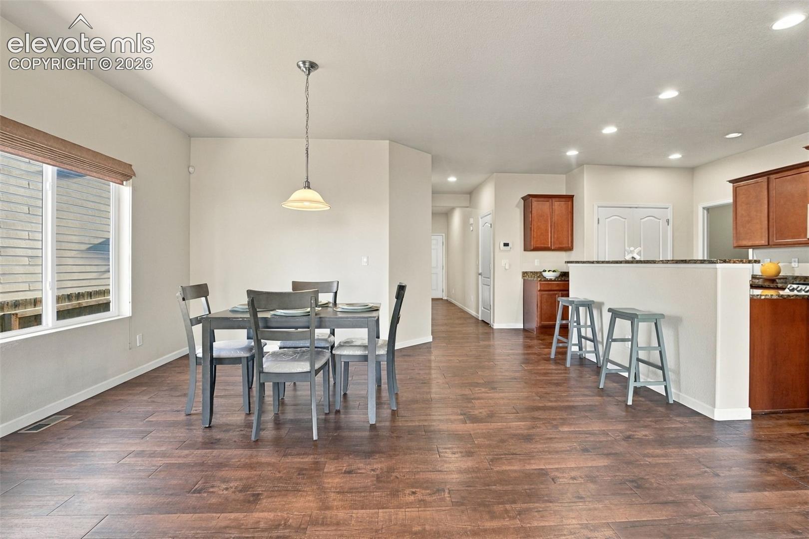 Open-concept interior featuring wood-finish flooring, recessed lighting, a neutral color palette, and dark-stained wood cabinetry with a breakfast bar