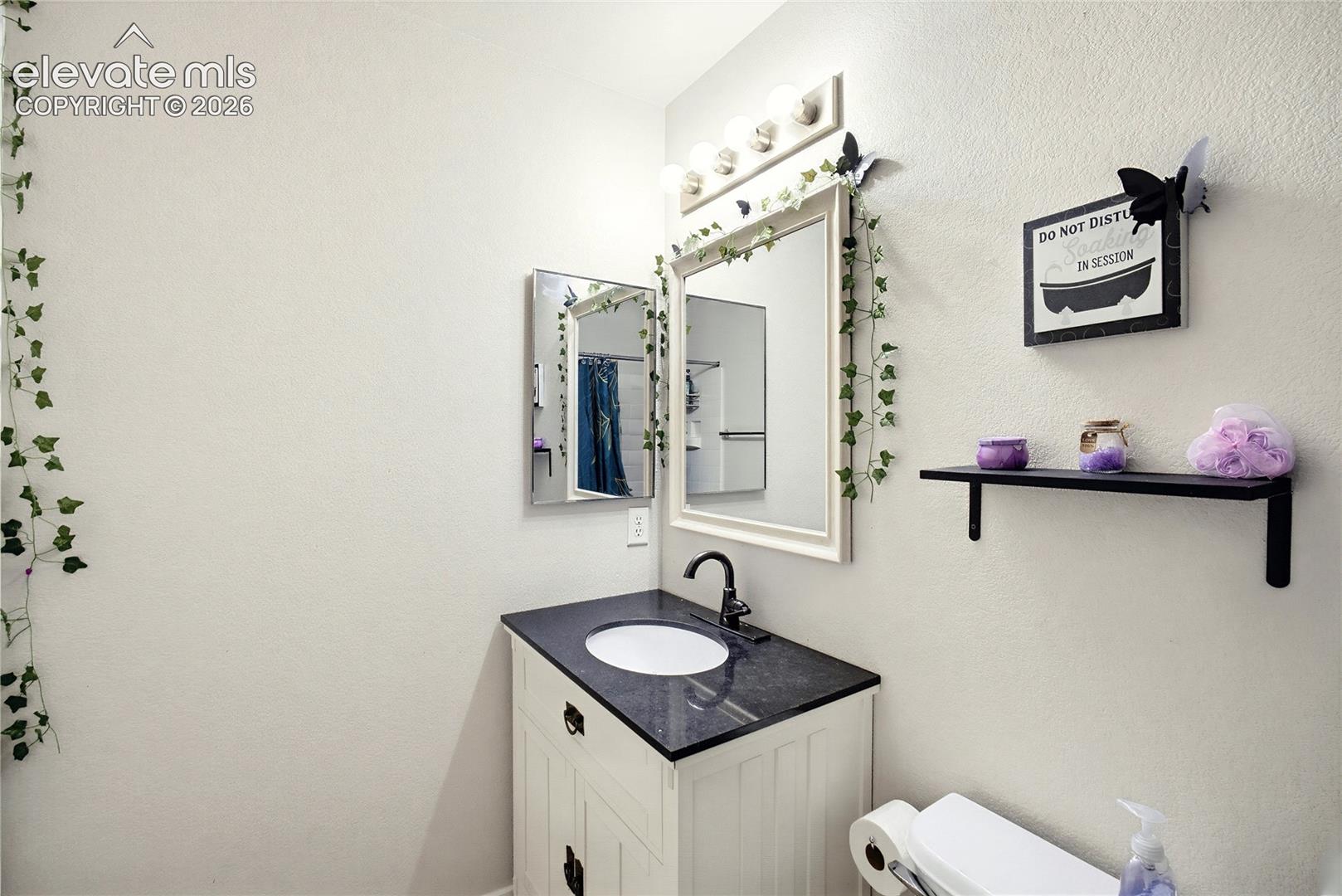 White vanity with dark countertop and integrated sink, framed mirror, and wall-mounted light fixture