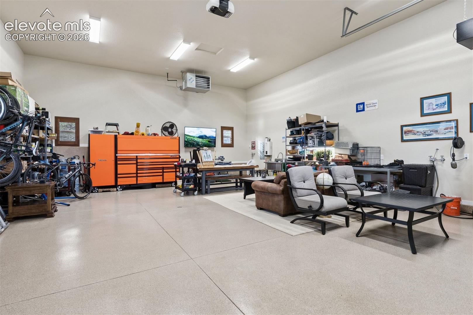 Oversized garage featuring a durable epoxy-coated floor, high-output overhead lighting, wall-mounted heater, and a dedicated utility sink