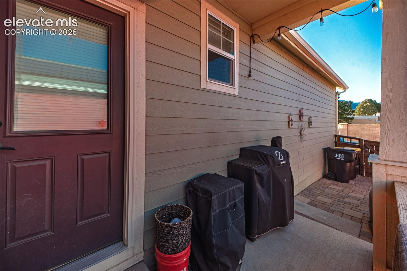 Covered patio featuring horizontal lap siding, paneled entry door, concrete flooring, and decorative string lighting