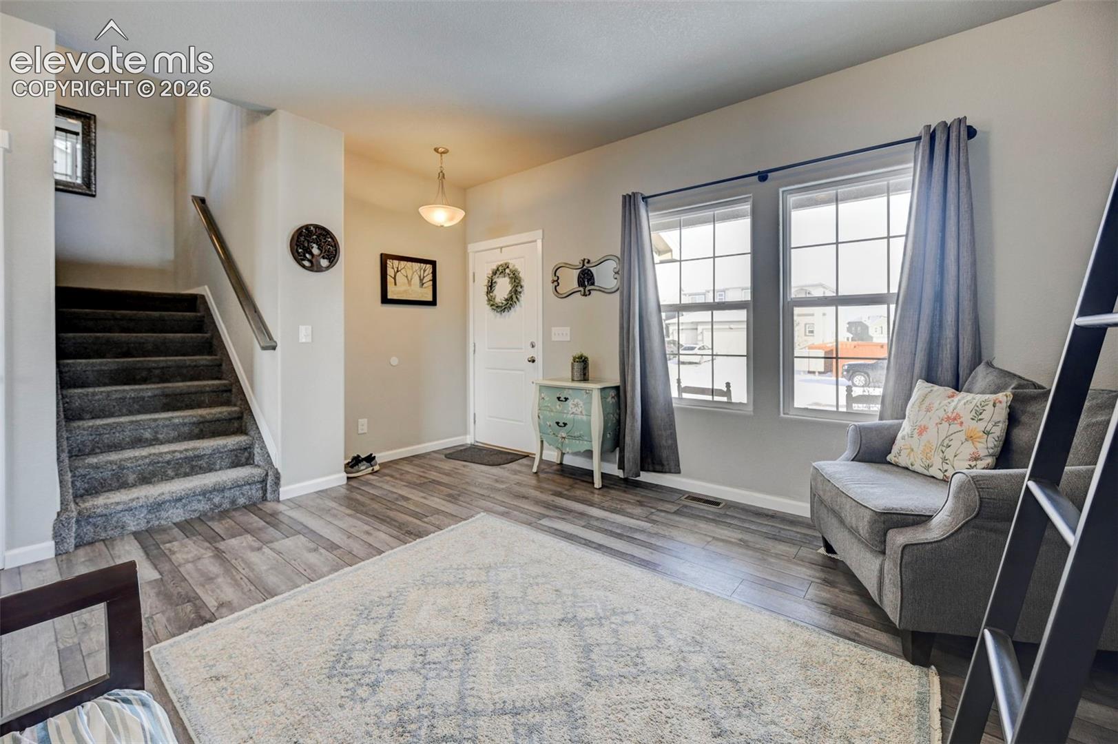 Entryway featuring wood-finish flooring, a staircase with carpeting, dual-pane windows with grid detailing, and a neutral color palette
