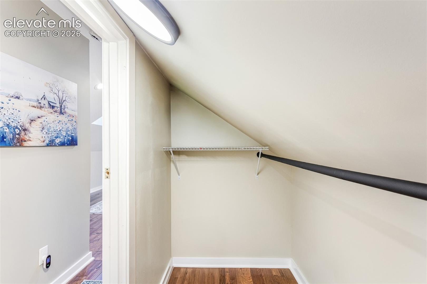 Sloped ceiling closet featuring wood-finish flooring, a metal hanging rod, and a wire shelf