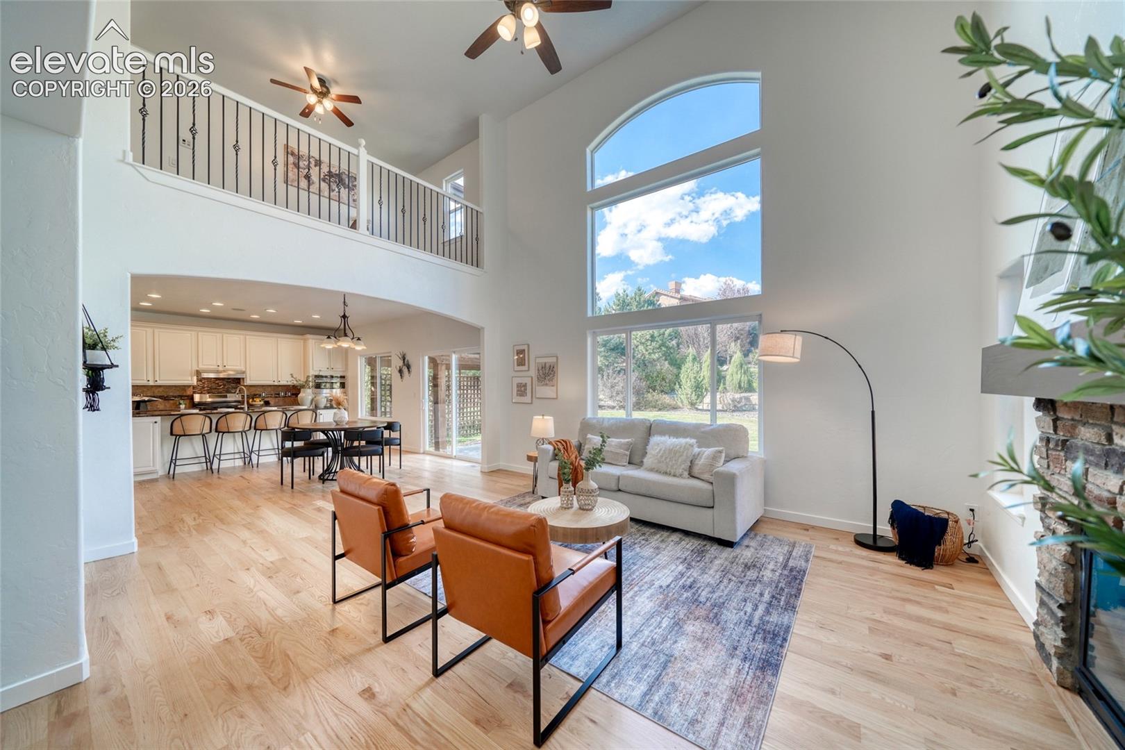 Two-story living area with hardwood flooring, a fireplace with stone surround, and an arched window