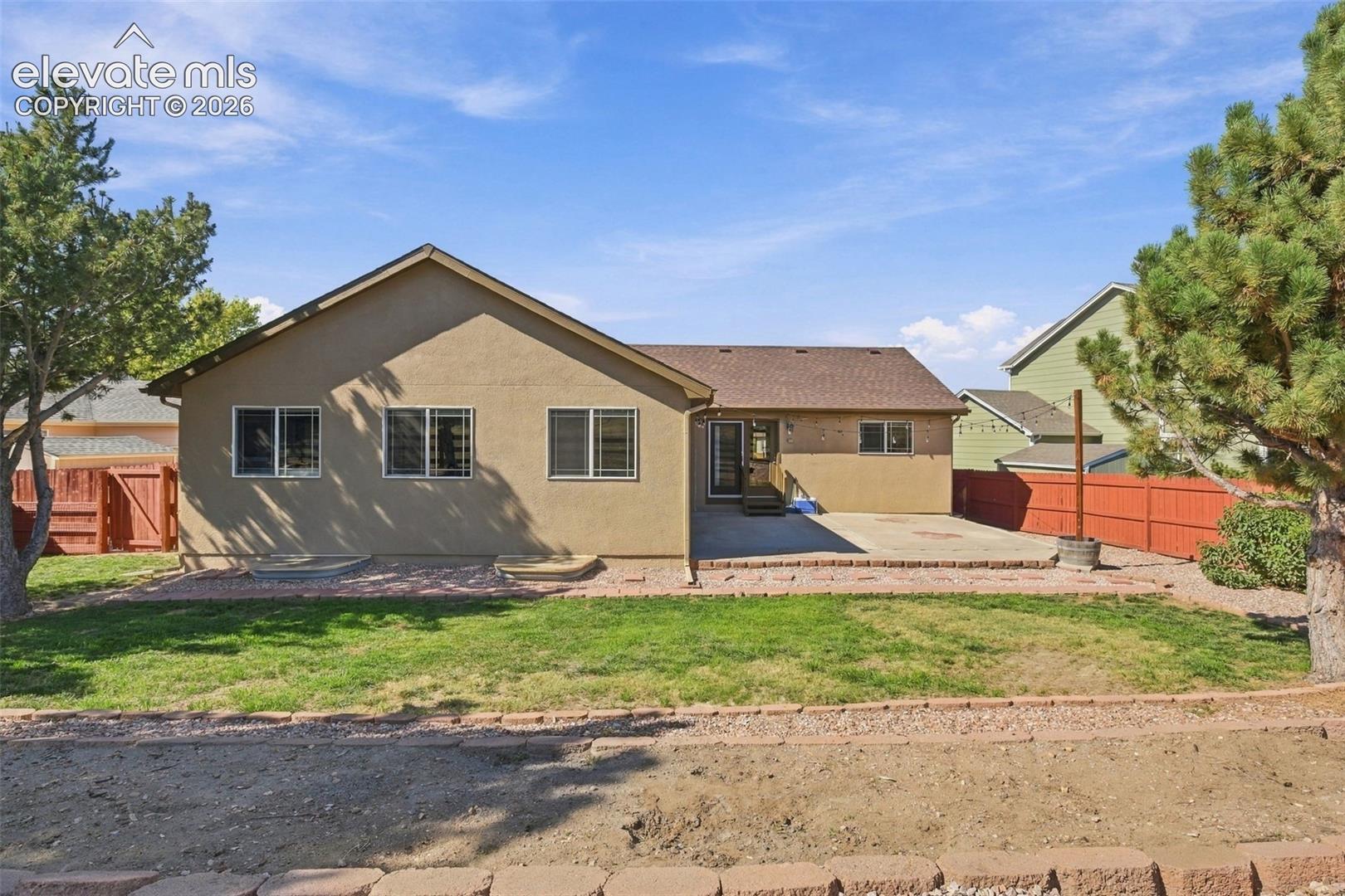 Expansive backyard featuring a concrete patio, mature trees, and a wooden privacy fence