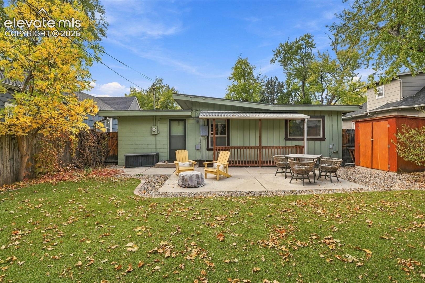 Rear exterior featuring a concrete patio, wood-railing covered porch, and detached storage shed within a fenced yard