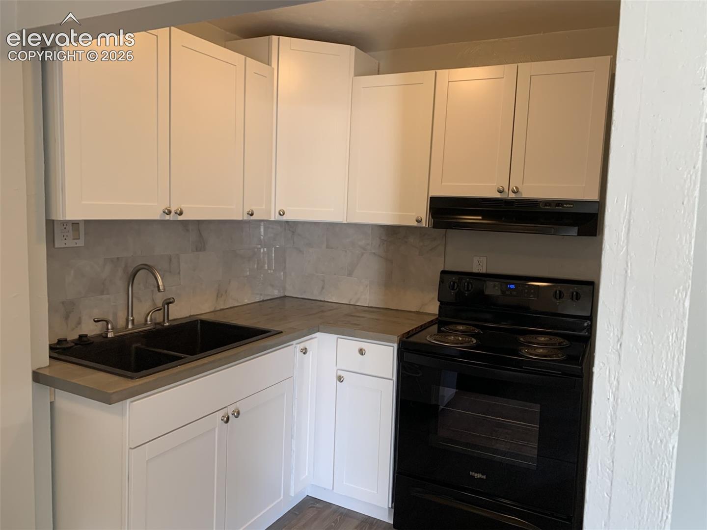 White shaker cabinetry, dark composite double basin sink, gray countertop, black electric range, and a gray tile backsplash
