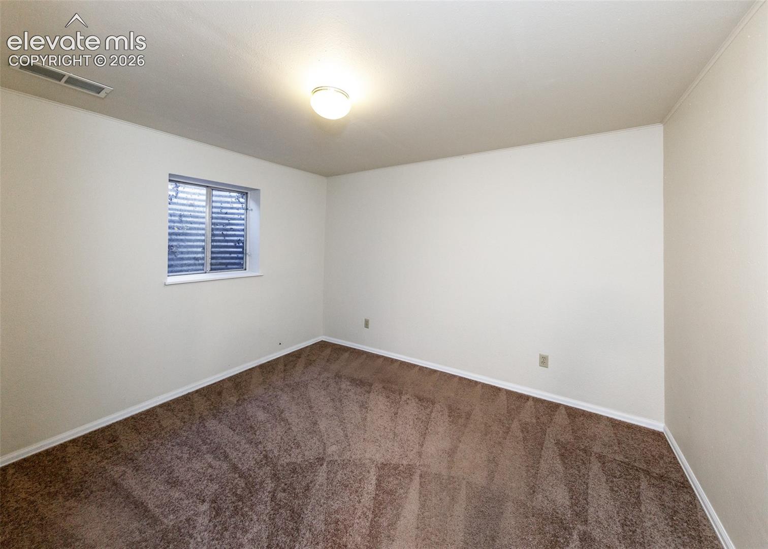 Neutral-toned interior space featuring wall-to-wall carpeting and a single egress window with an exterior well cover