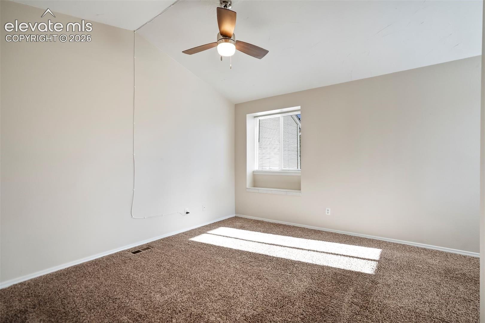 Vaulted ceiling, neutral wall tones, inset window with sill, and ceiling fan with integrated light fixture