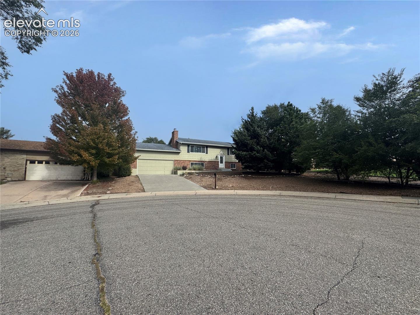 Split-level exterior featuring a brick and siding facade, chimney, concrete driveway, and attached garage