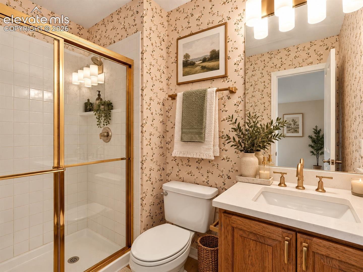 Bathroom featuring a vanity with a white solid-surface countertop, an undermount rectangular sink, brass-finish hardware, a shower enclosure with gold-toned framing, and white tiled shower walls