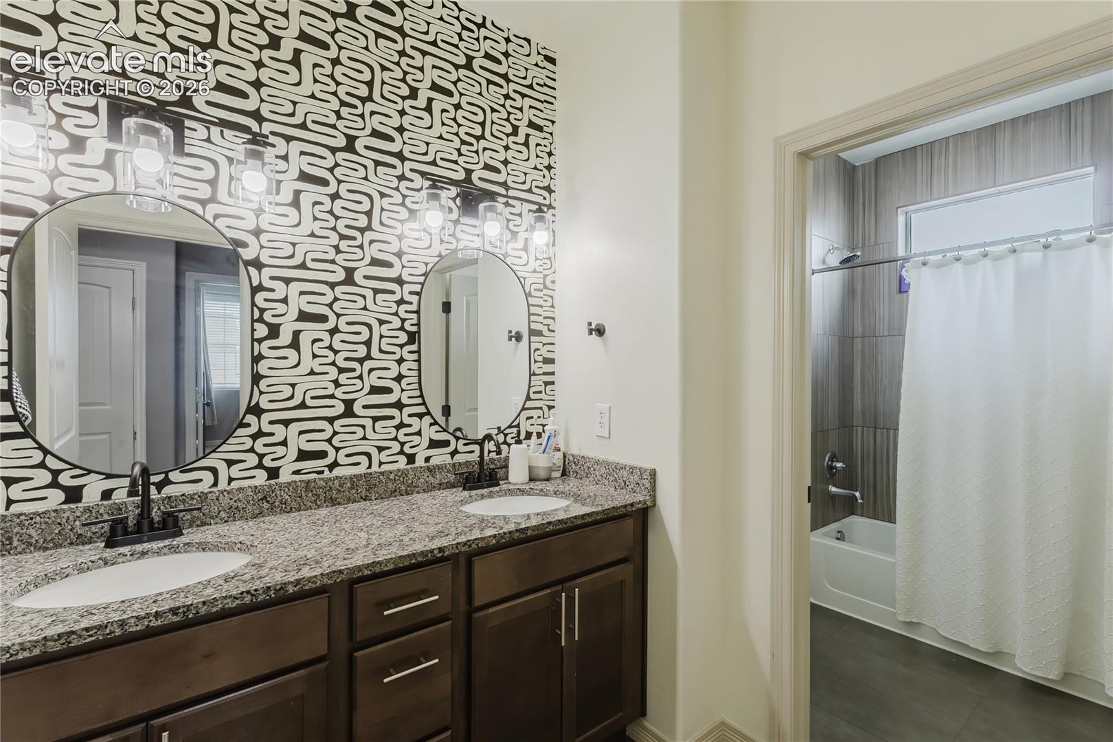 Dual vanity with granite countertop, undermount sinks, matte black fixtures, and decorative accent wall