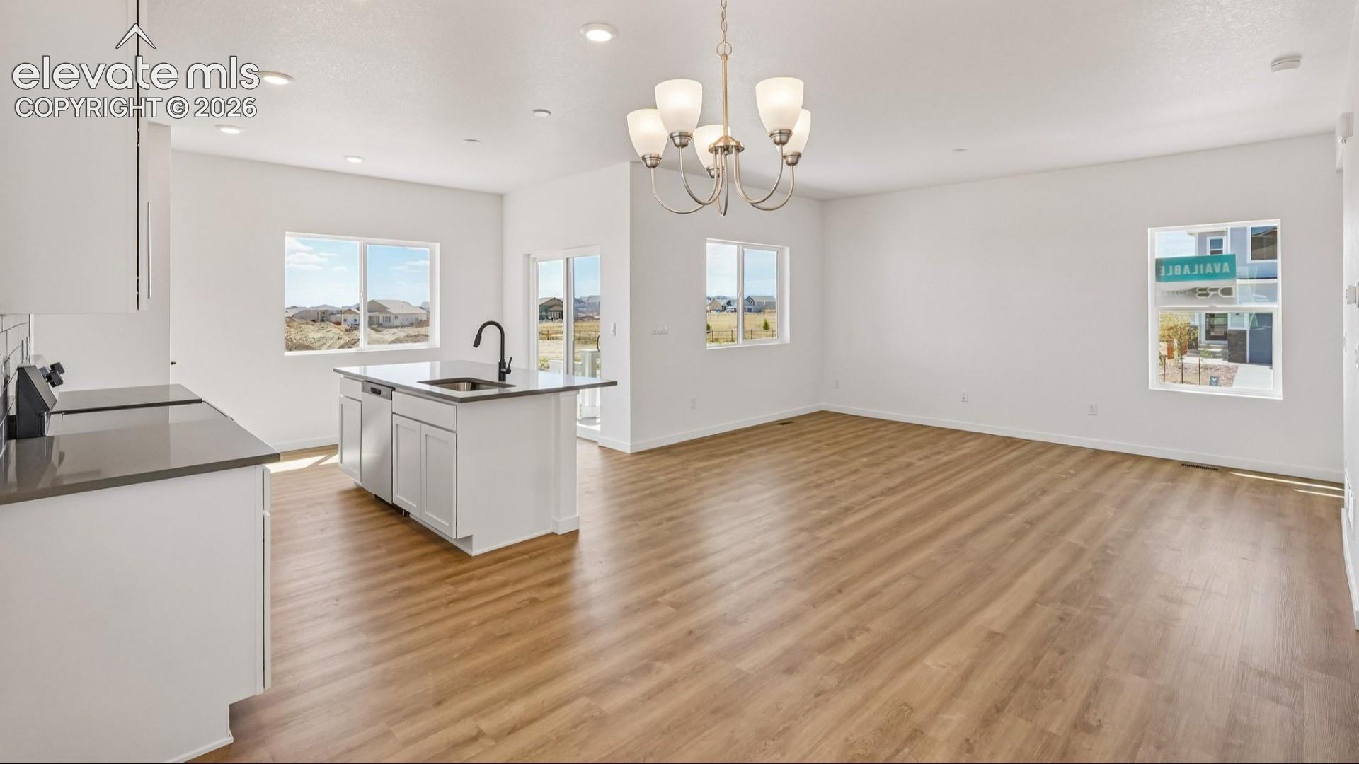 Open-concept space featuring wood-finish flooring, a kitchen island with stone-finish countertops, recessed lighting, and a multi-arm chandelier