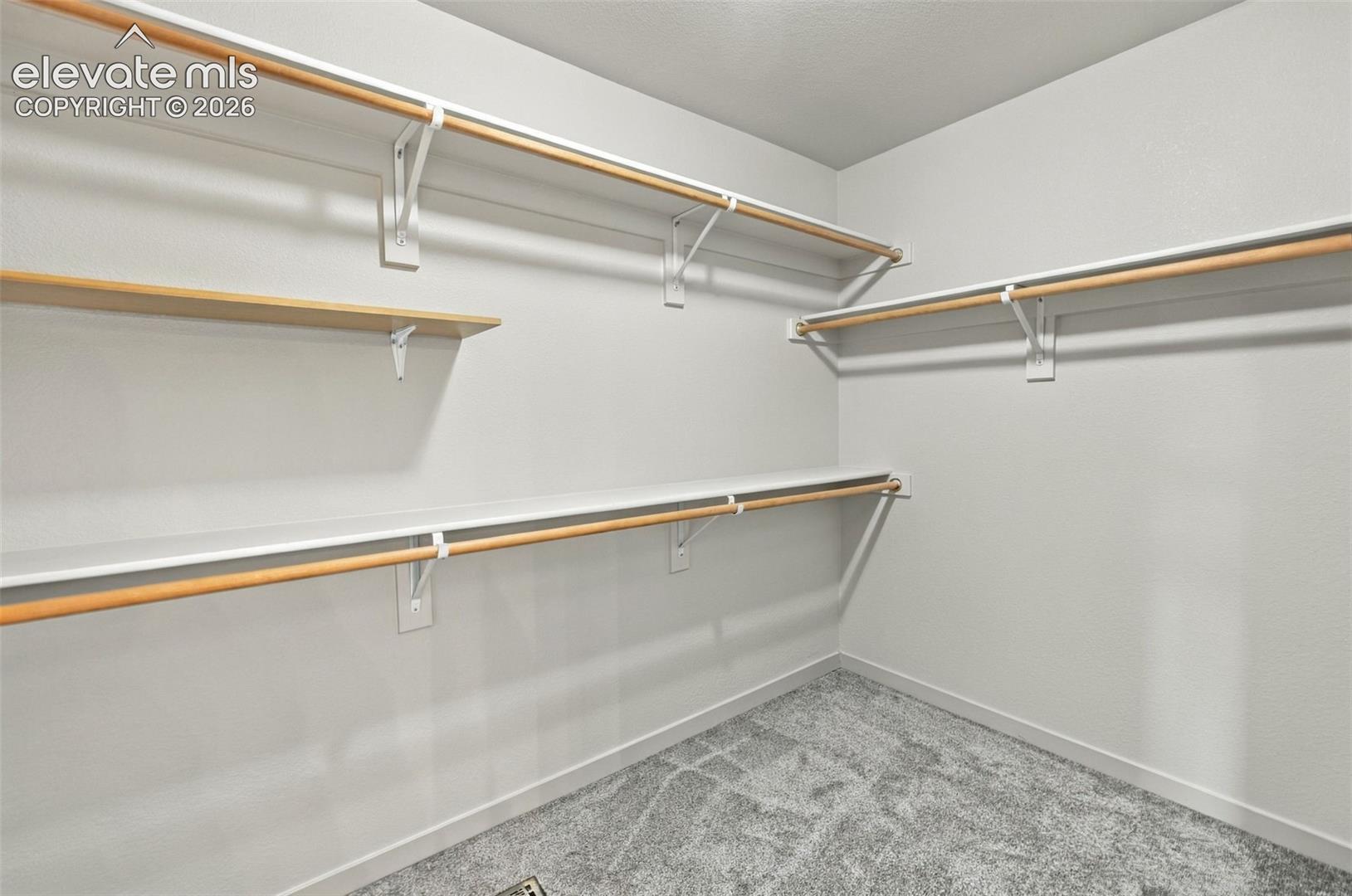 Storage area featuring multi-level white shelving and integrated wooden garment rods