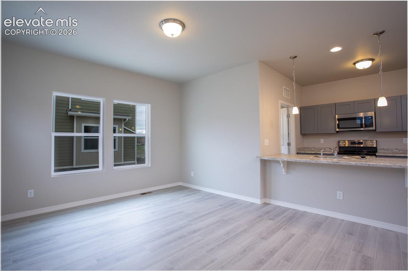 living room with two side-by-side windows and open view into a kitchen with pendant lights and a breakfast bar