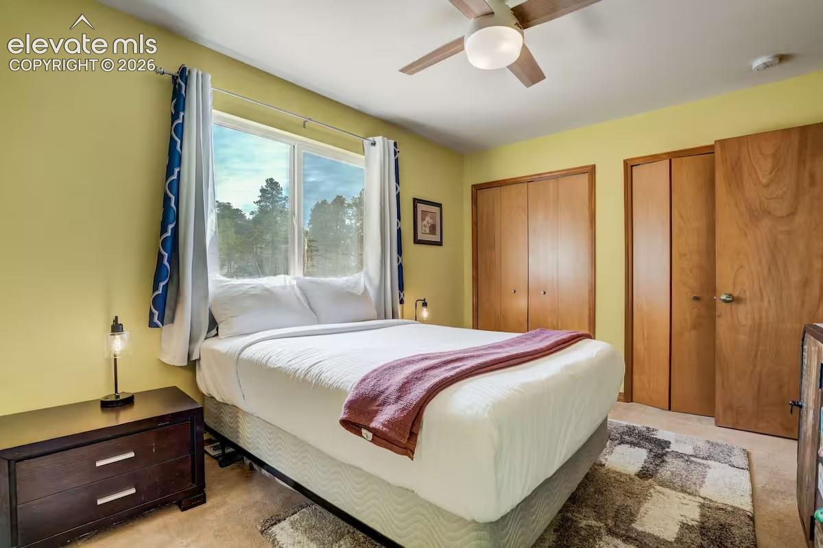 Bedroom featuring a large window, light wood-finish doors, a ceiling fan with integrated lighting, and carpet flooring