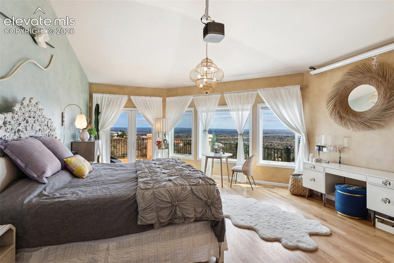 Vaulted ceiling bedroom featuring wood-finish flooring, a decorative chandelier, built-in vanity, and multiple windows with a prominent exterior landscape