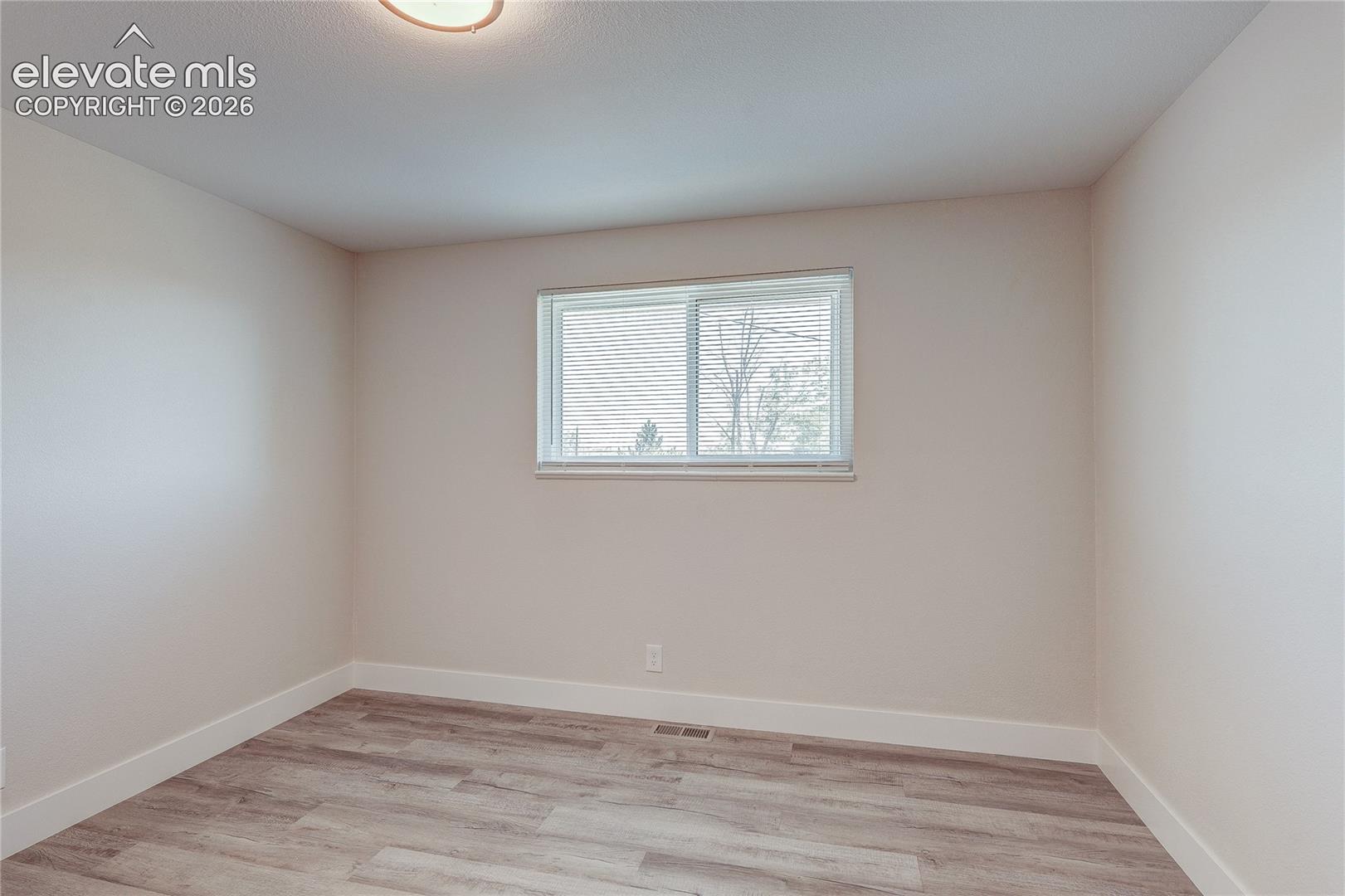 Neutral interior featuring light-toned walls, wood-finish flooring, a sliding window, and a flush-mount ceiling light