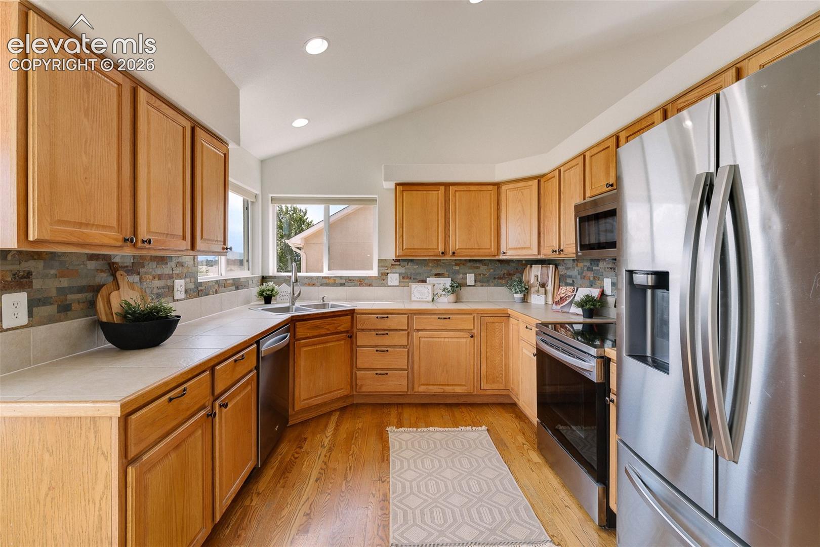 Kitchen featuring wood-finish cabinetry, stainless steel appliances, a tile backsplash, light-colored countertops, and wood-finish flooring