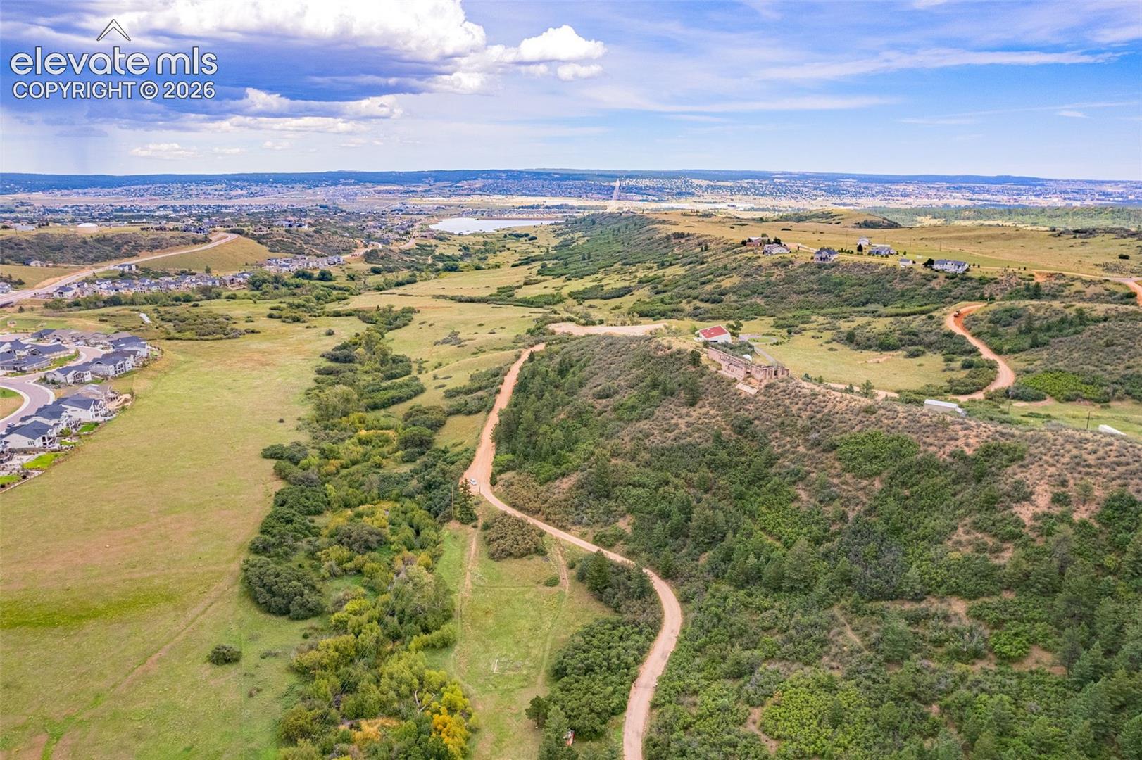 Expansive natural landscape featuring rolling hills, scattered trees, and distant bodies of water