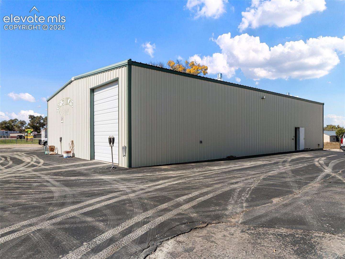 Steel-frame structure featuring corrugated metal siding, a wide roll-up bay door, an entry door, and an expansive asphalt parking surface